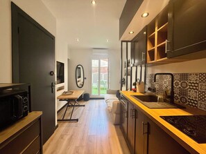A compact kitchen with a microwave, stove, and a small dining area. - B087 Appartement cosy et moderne – Terrasse-Centre-ville (Cannes)