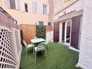 A small outdoor patio with a table and chairs, surrounded by a wooden fence and a hedge. - B087 Appartement cosy et moderne – Terrasse-Centre-ville (Cannes)