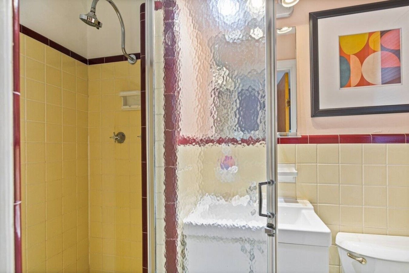 A bathroom with a glass shower enclosure, a toilet, and a framed abstract painting on the wall.