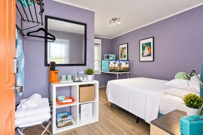 Habitación de hotel moderna con cama, escritorio con computadora, televisión y zona de baño con toallero y ducha.