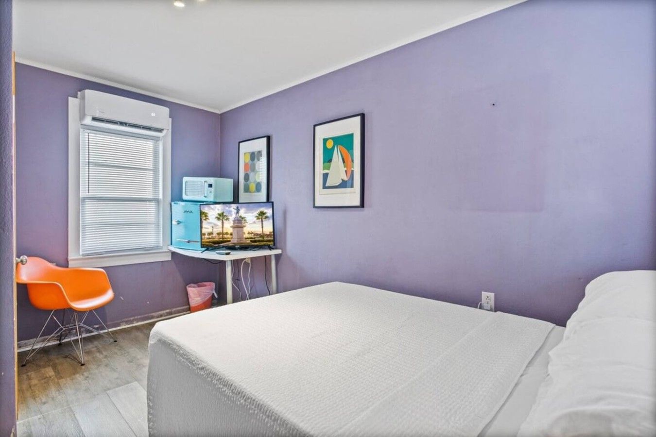 A bedroom with a bed, a desk with a computer, a chair, and a window with blinds.