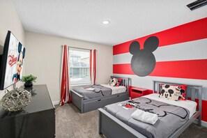 A bedroom with two beds, a Mickey Mouse mural, and a Disney poster. - 4BR Champions Gate Villa | Oasis Club Amenitie’s (Kissimmee)