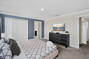 Un dormitorio con una cama, un tocador, un televisor y una puerta que da a otra habitación.