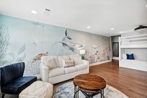 A room with a mural of marine life, a sofa, a chair, a small table, and a white shelving unit. - 30A Upscale Villa | Coastal Charm & Beach Access (Santa Rosa Beach)