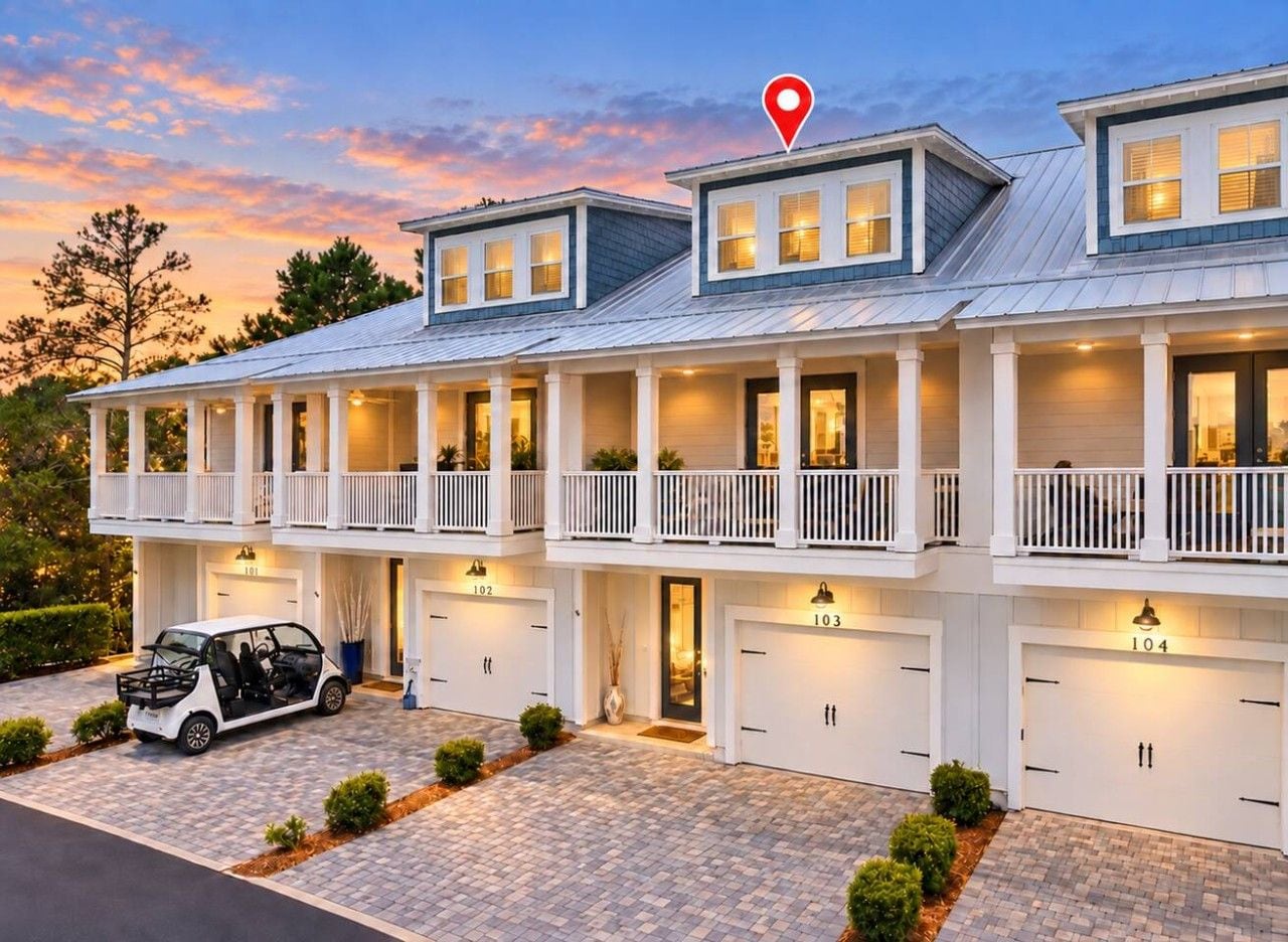 A multi-story residential building with a garage, a car parked in front, and a red location marker.