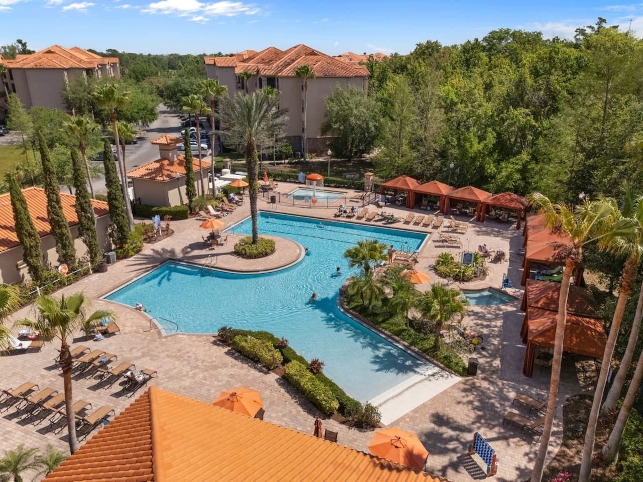 A resort with a central swimming pool, lounge areas, and palm trees.