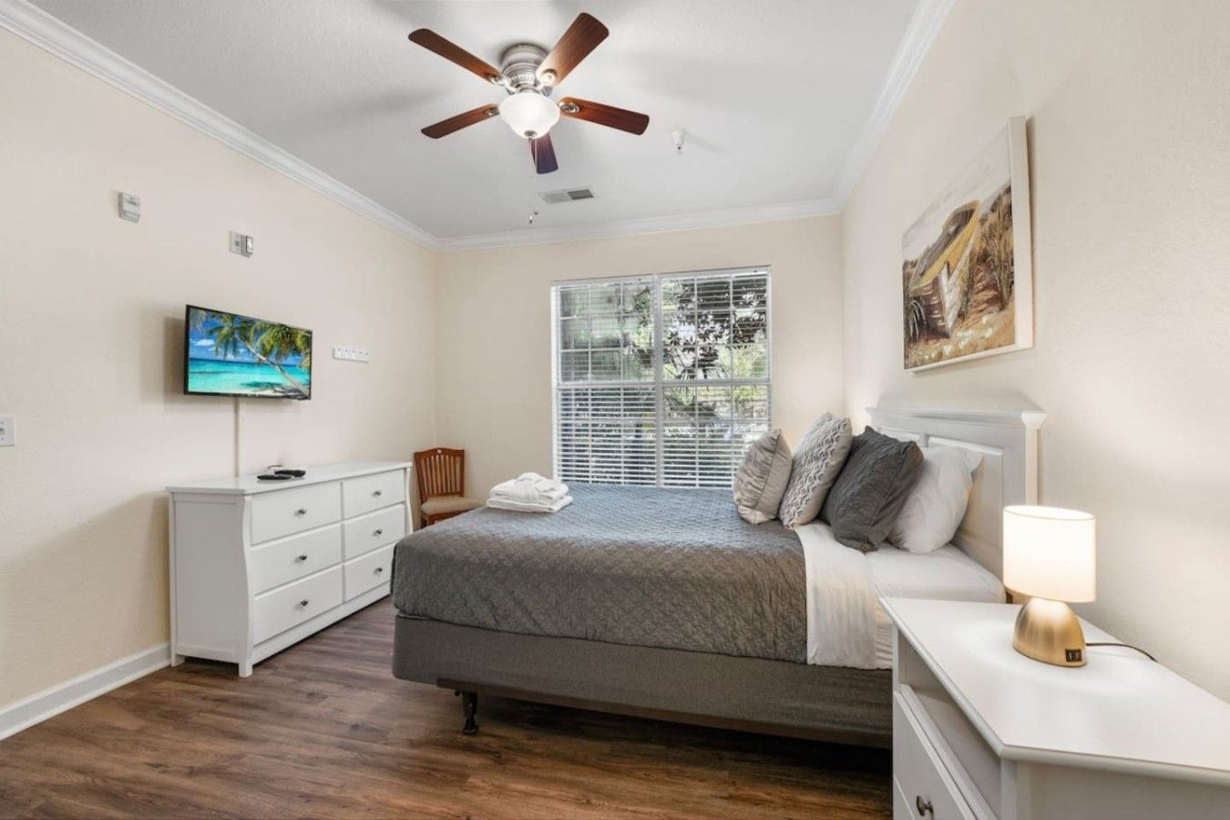 A bedroom with a bed, a nightstand, a TV, a ceiling fan, and a window with blinds.