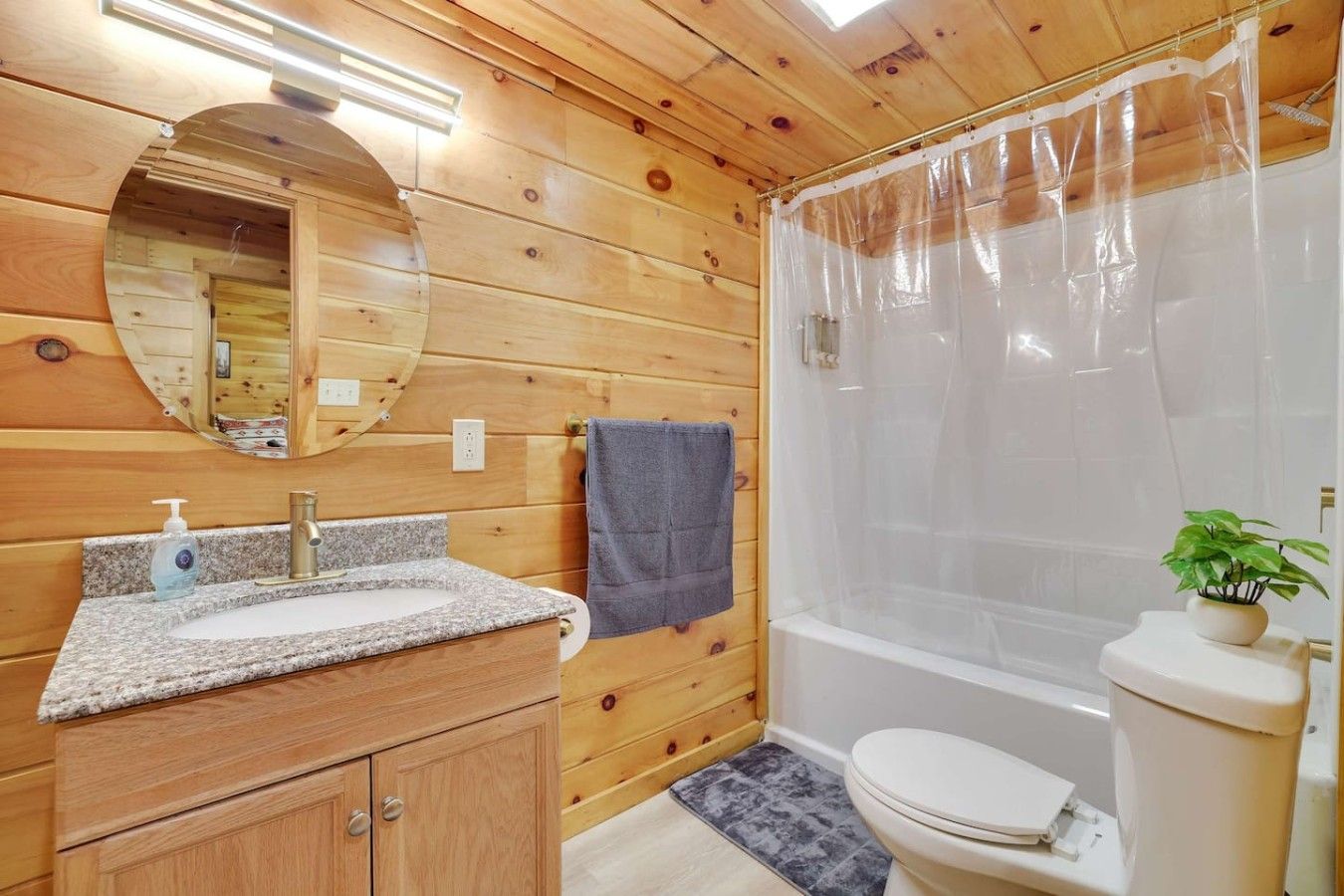 A wooden cabin bathroom with a granite sink, a mirror, a shower curtain, and a toilet.