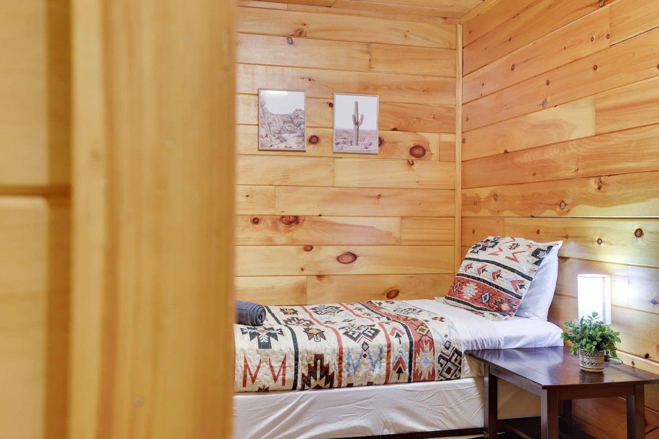 Ein Zimmer einer Holzhütte mit einem Bett, einem Nachttisch und zwei gerahmten Bildern an der Wand.