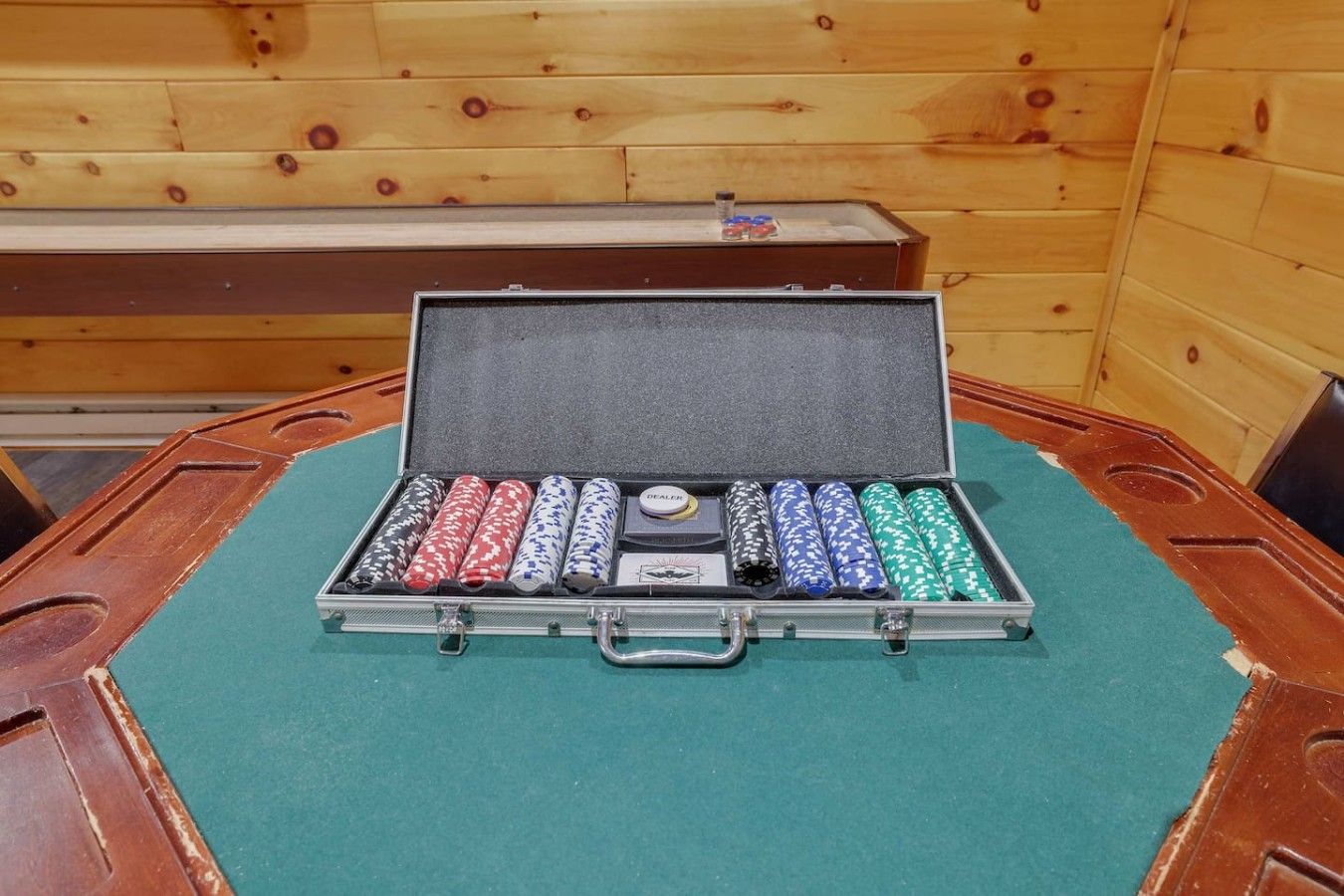 Ein Pokertisch mit grünem Filz und einer Box mit Pokerchips und einem Dealer-Button.