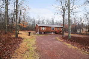 A log cabin with a red door, surrounded by a forest with leaf-covered ground.