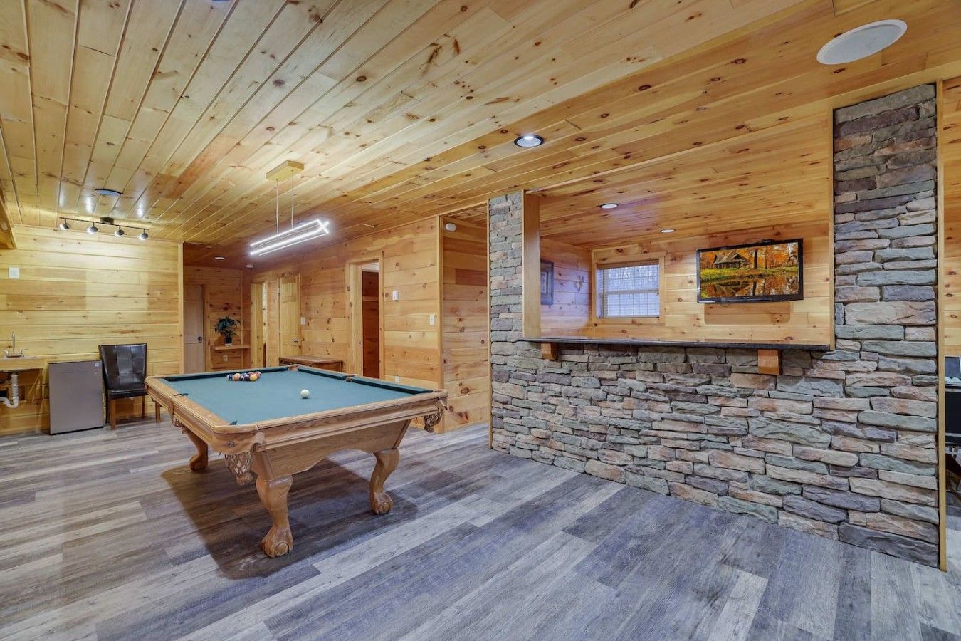 Un interior de madera con una mesa de billar, pared de piedra y un cuadro enmarcado.