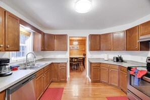 Una cocina con armarios de madera, lavavajillas, fregadero y una zona de comedor con mesa y sillas.