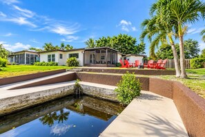A residential property with a swimming pool, outdoor seating, and a well-maintained lawn. - Fort Myers Waterfront Retreat | 4BR Home W/Views (Fort Myers)