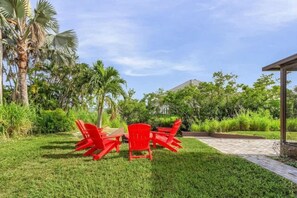 A patio area with a table and chairs, surrounded by lush greenery and a clear sky. - Fort Myers Waterfront Retreat | 4BR Home W/Views (Fort Myers)