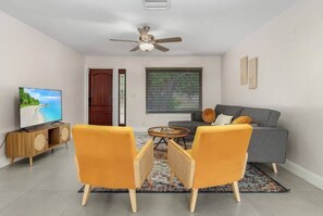 A living room with a sofa, two armchairs, a coffee table, a TV, and a ceiling fan. - Fort Myers Waterfront Retreat | 4BR Home W/Views (Fort Myers)