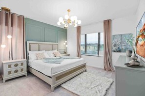 A bedroom with a bed, nightstands, a chandelier, a window with blinds, and a painting on the wall. - Super Ritzy 9BR | Ultimate Disney Retreat (Orlando)