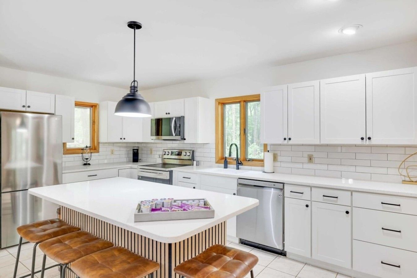 A modern kitchen with white cabinetry, stainless steel appliances, and a central island with stools.