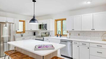 A modern kitchen with white cabinetry, stainless steel appliances, and a central island with stools.