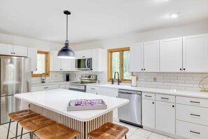 Eine moderne Küche mit weißen Schränken, Edelstahlgeräten und einer zentralen Kochinsel mit Sitzgelegenheiten.