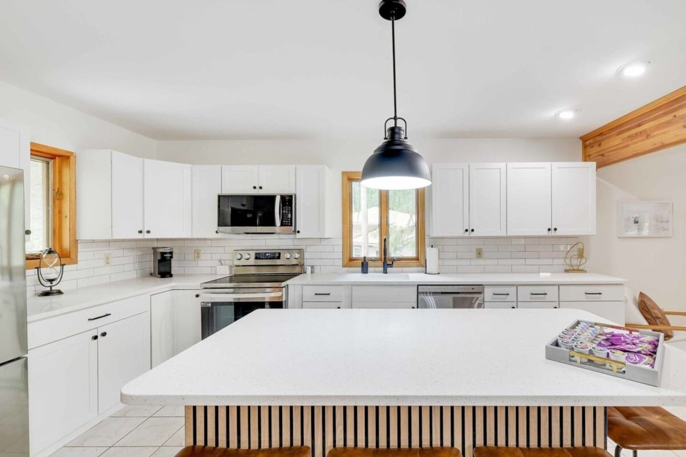A modern kitchen with white cabinetry, a central island, and a black pendant light.