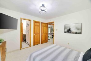 A bedroom with a bed, a TV, a painting, and a ceiling fan.
