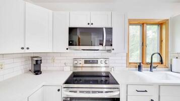 A modern kitchen with white cabinetry, a built-in microwave, an oven, and a window with a view of trees.