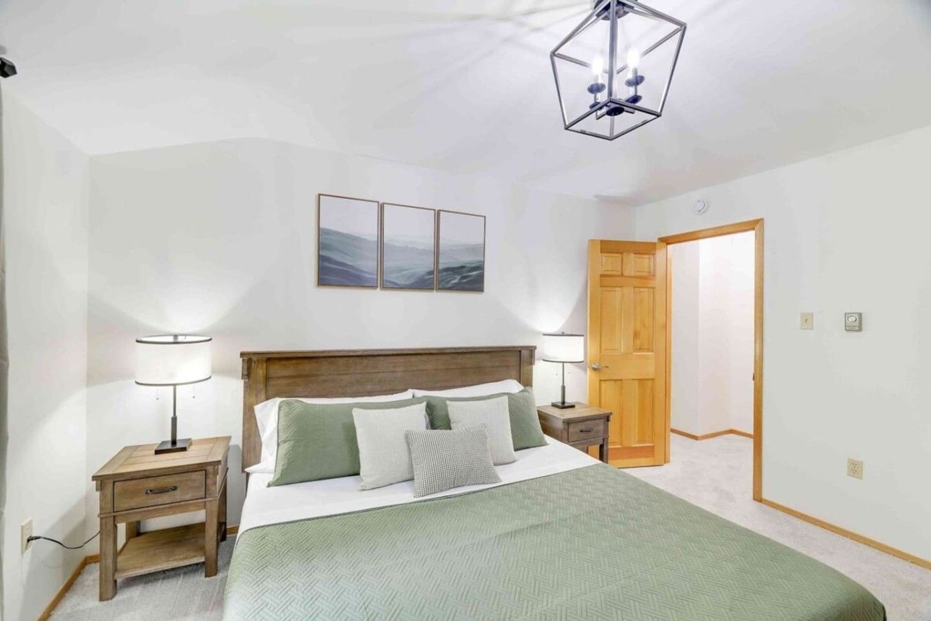 A bedroom with a bed, bedside tables, a wooden door, and a ceiling light fixture.