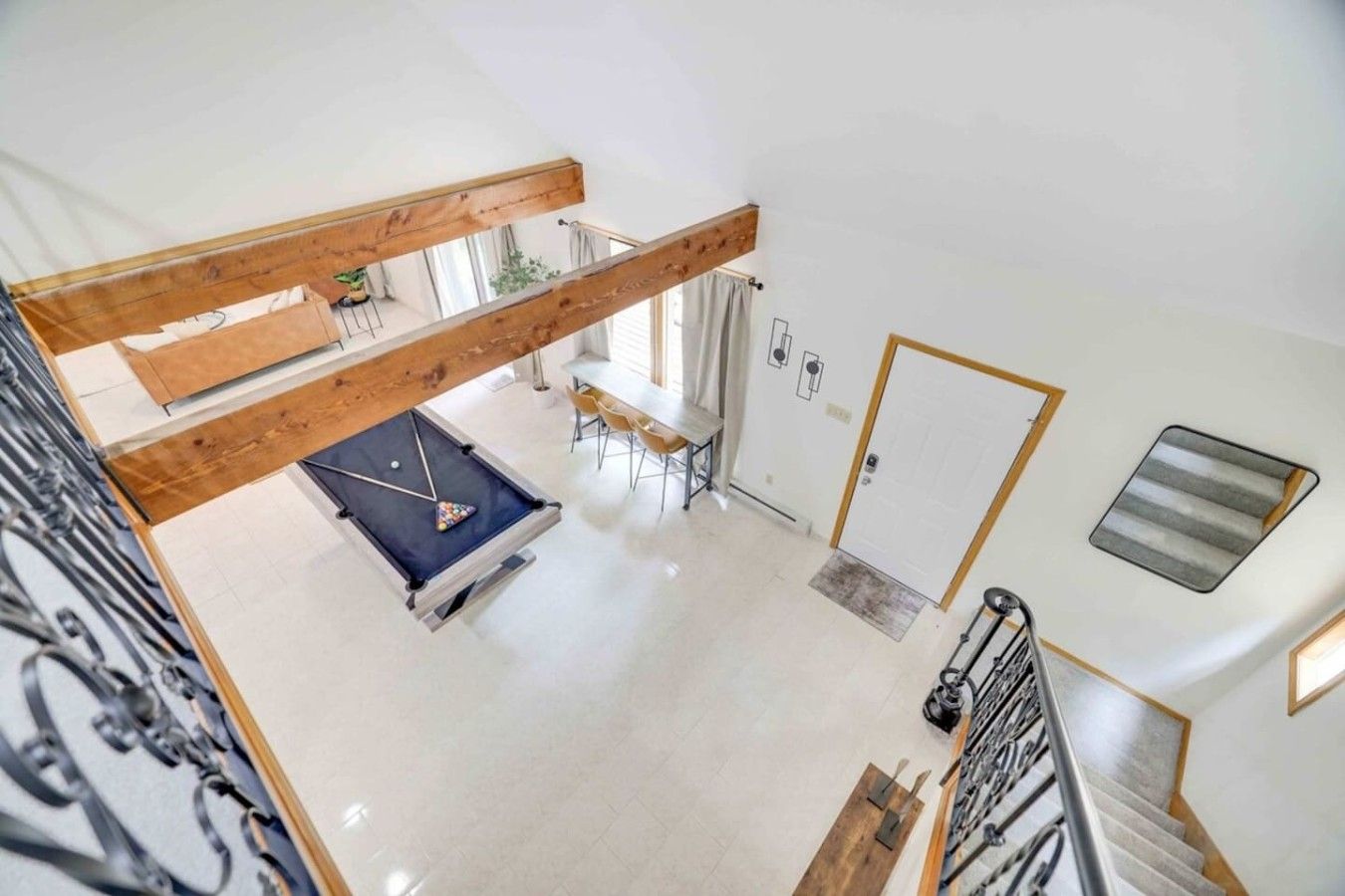 A high-ceilinged room with a pool table, a staircase, and a door leading to another area.