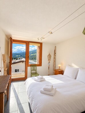 A bedroom with a bed, a chair, a nightstand, and a view of a mountain landscape. - Foppa Alpine Lodge – Ski-in/Ski-out & Sauna (Valbella)