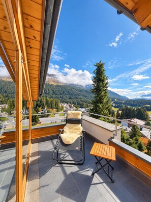 Ein Balkon mit Blick auf eine gebirgige Landschaft, einem Liegestuhl und einem kleinen Tisch.