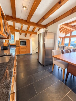 Eine moderne Küche mit einem Edelstahlkühlschrank, Holzschränken und einem Essbereich mit Tisch und Stühlen.