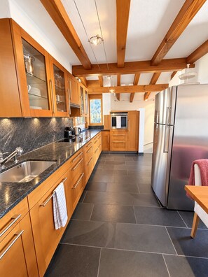 A modern kitchen with wooden cabinets, a stainless steel refrigerator, and a granite countertop. - Foppa Alpine Lodge – Ski-in/Ski-out & Sauna (Valbella)