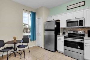 A compact kitchen with a refrigerator, microwave, stove, and a small dining area with chairs and a table. - Regal Palms Villa | Lazy River | Slides | Arcade | (Davenport)