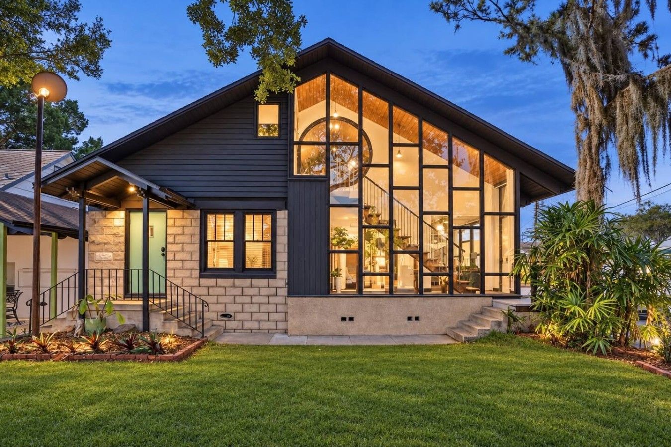A modern house with a large glass facade, a visible staircase, and a well-maintained lawn.