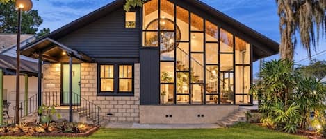 Et moderne hus med stor glasfacade, synlig trappe og velplejet græsplæne.