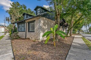 A two-story house with a stone facade, a small front yard with mulch, and a banana tree. - Pet-Friendly St. Augustine Getaway | Cozy Bungalow (St. Augustine)