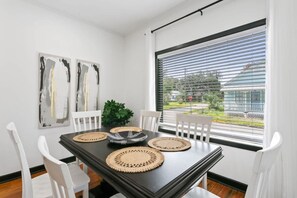 A dining area with a black table, white chairs, and two abstract paintings on the wall. - Pet-Friendly St. Augustine Getaway | Cozy Bungalow (St. Augustine)