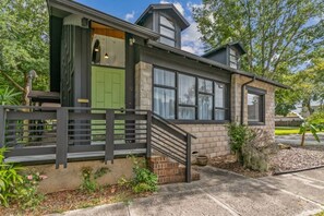 A modern two-story house with a green door, a brick exterior, and a small front porch with a black railing. - Pet-Friendly St. Augustine Getaway | Cozy Bungalow (St. Augustine)