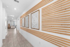 A hallway with a wooden slat wall design, a tiled floor, and framed artwork. - 6BR Champions Gate Villa | w/Oasis Club Amenities! (Davenport)