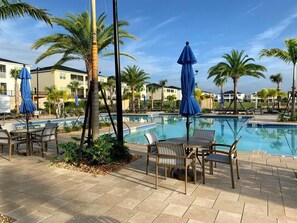 A pool area with lounge chairs and umbrellas, surrounded by palm trees and buildings. - 6BR Champions Gate Villa | w/Oasis Club Amenities! (Davenport)