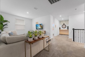 Ein modernes Wohnzimmer mit einer Couch, einem Couchtisch mit Pflanzen, einem Fernseher und einer Treppe zu einer weiteren Ebene.
