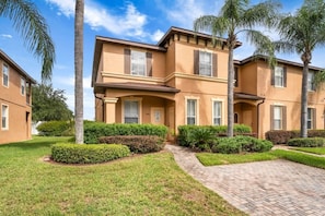 A two-story residential building with a brick pathway leading to the entrance, surrounded by well-maintained hedges and palm trees. - Regal Palms Villa | Lazy River | Slides | Games (Davenport)