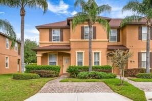 A two-story residential building with a brick pathway leading to the entrance, surrounded by well-maintained hedges and palm trees. - Regal Palms Villa | Lazy River | Slides | Games (Davenport)