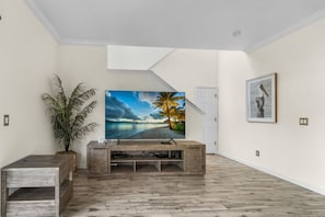 A living room with a wooden entertainment unit, a large flat-screen TV, a potted plant, and a framed artwork on the wall. - Regal Palms Villa | Lazy River | Slides | Games (Davenport)