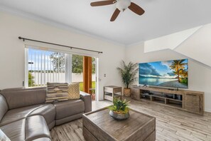 A modern living room with a leather sofa, a coffee table with a plant, a TV on a wooden stand, and a ceiling fan. - Regal Palms Villa | Lazy River | Slides | Games (Davenport)