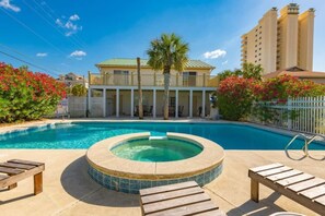 Une piscine avec un jacuzzi, une terrasse en bois et un bâtiment doté d’un balcon en arrière-plan.