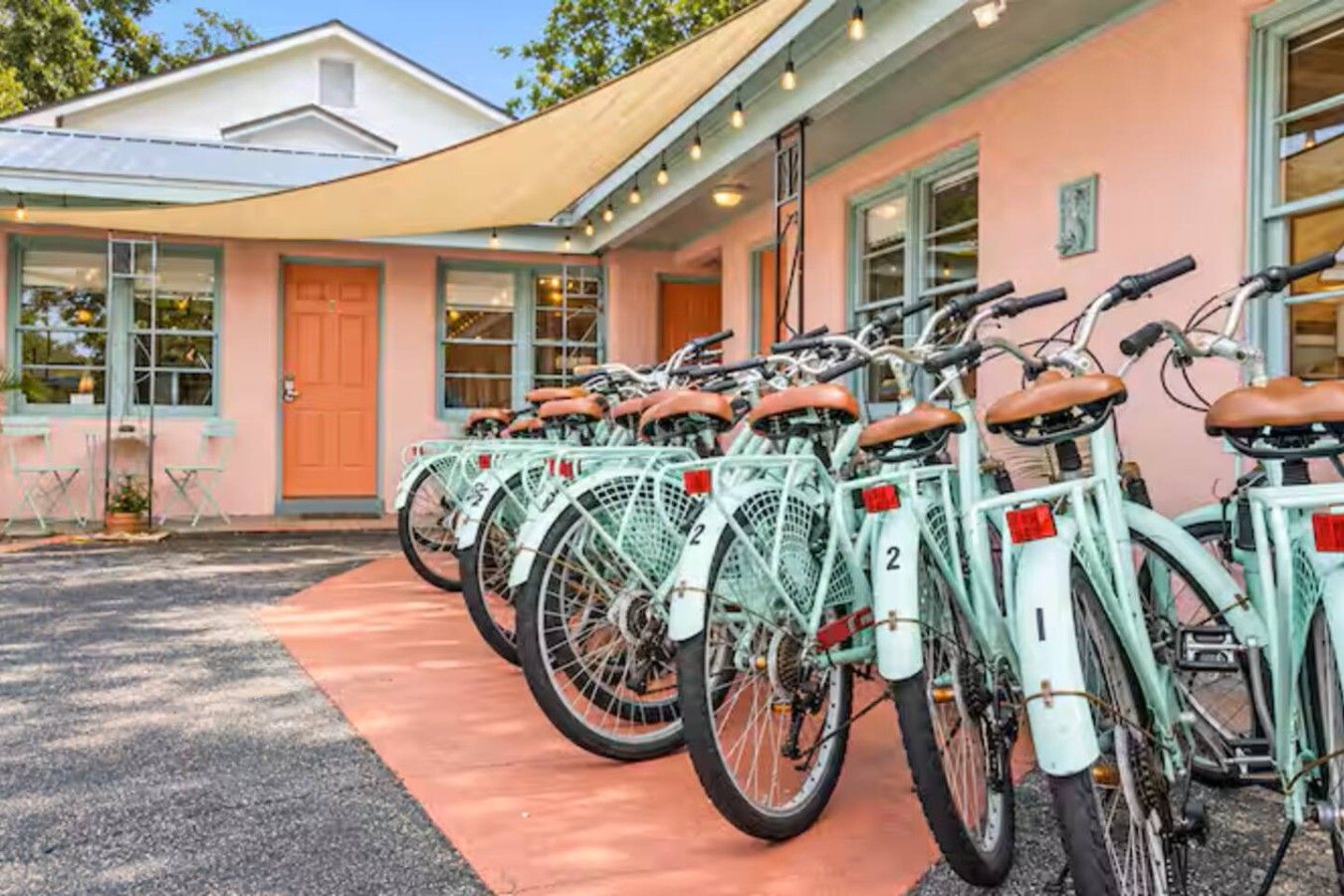 Une rangée de vélos numérotés est garée devant un bâtiment à la façade rose et à l’entrée abritée.