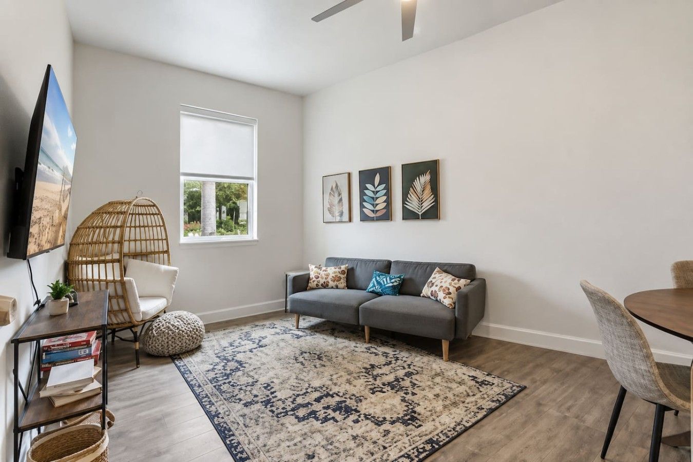 A modern living room with a grey sofa, a round table, a television, and a large window.