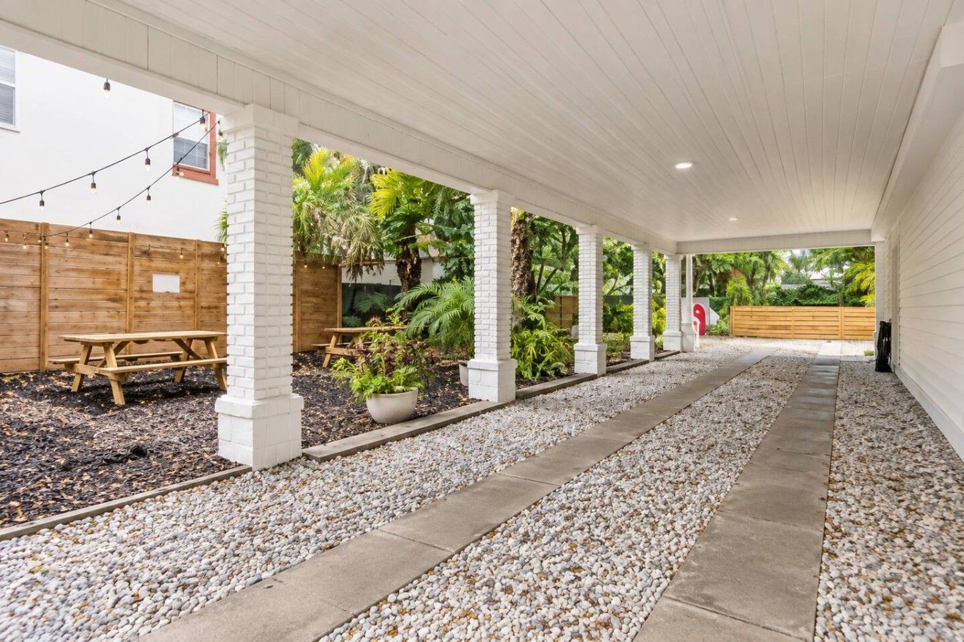 A covered outdoor area with a gravel pathway, wooden benches, and potted plants.